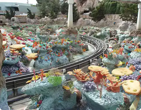 Miniature train track winding through a colorful coral reef-themed landscape outdoors.